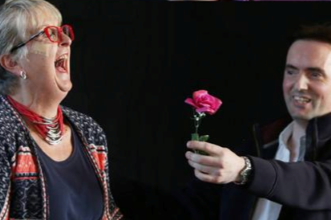 The Impossible Mr Goodwin holding a Rose on stage with a lady laughing